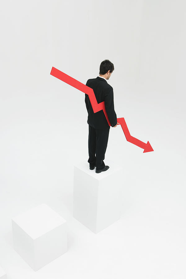 Businessman standing at top of steps holding arrow pointed downward Photograph by PhotoAlto/Milena Boniek