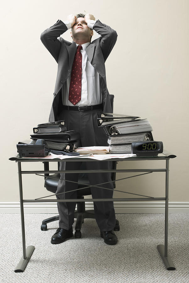 Businessman standing behind a desk with his hands on his head Photograph by Photodisc