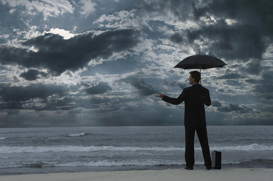 Businessman Standing on a Beach at Night, Holding an Umbrella and Checking for Rain Photograph by John Cumming