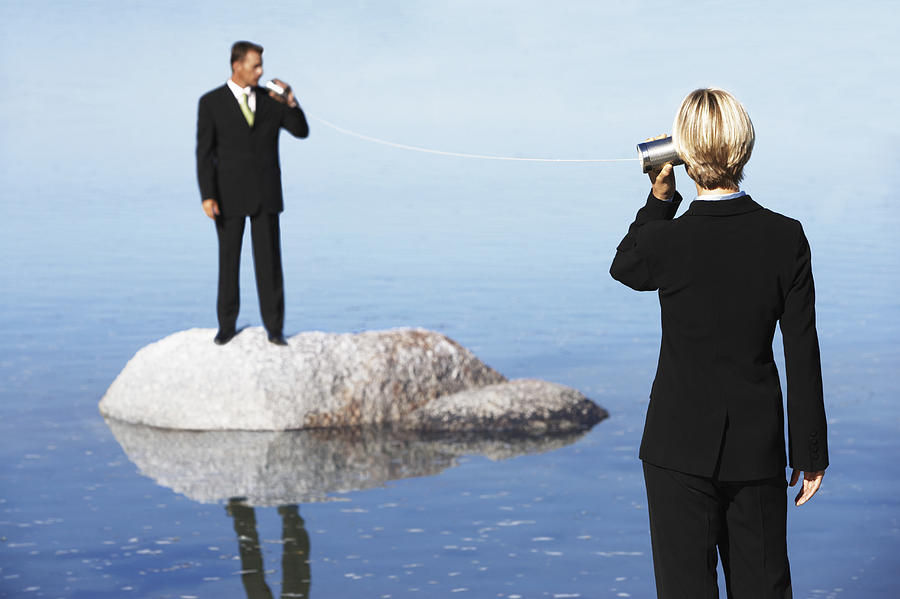 Businessman Standing on a Rock in the Sea, Talking to a Businesswoman Through Two Tin Cans Connected by String Photograph by John Cumming