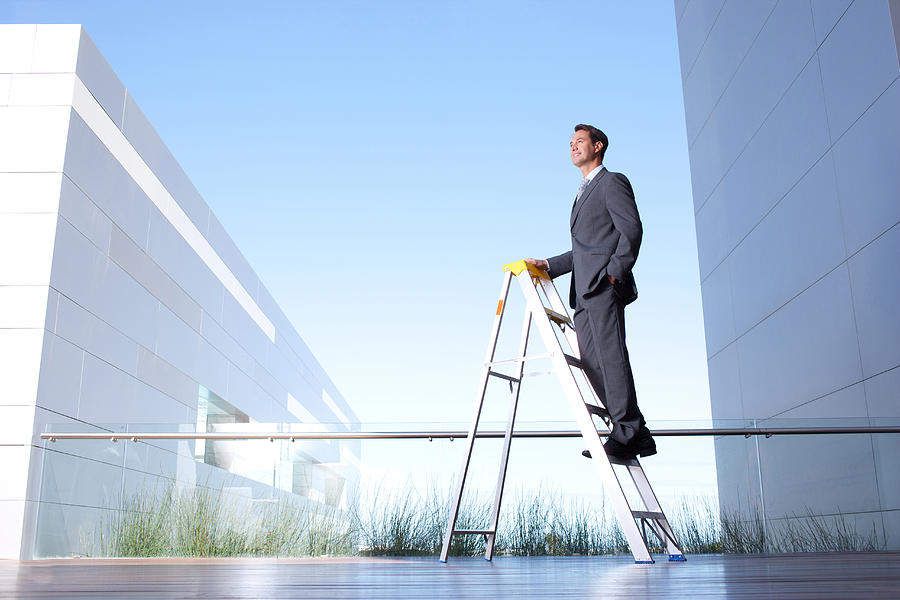 Businessman standing on ladder on balcony Photograph by Martin Barraud