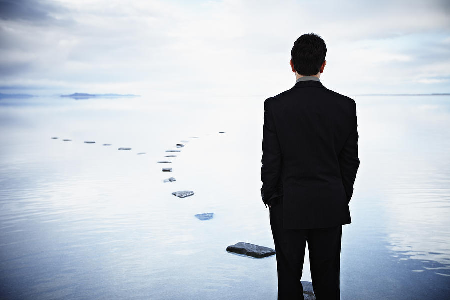 Businessman standing on stone pathway in water Photograph by Thomas Barwick