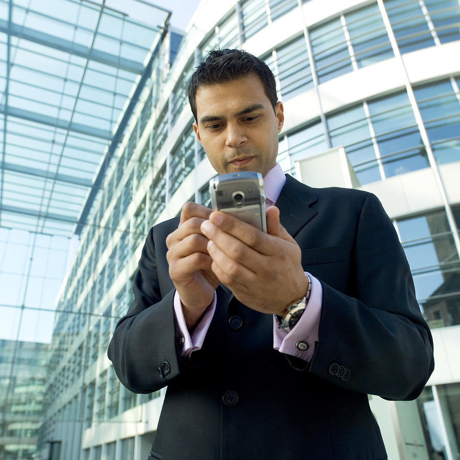 Businessman Standing Outside a Glass Building, Using a Handheld PC Photograph by Bloom Productions