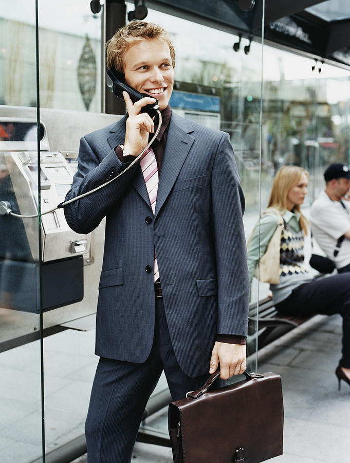 Businessman Stands by a Bus Stop Talking on a Payphone Photograph by Digital Vision.