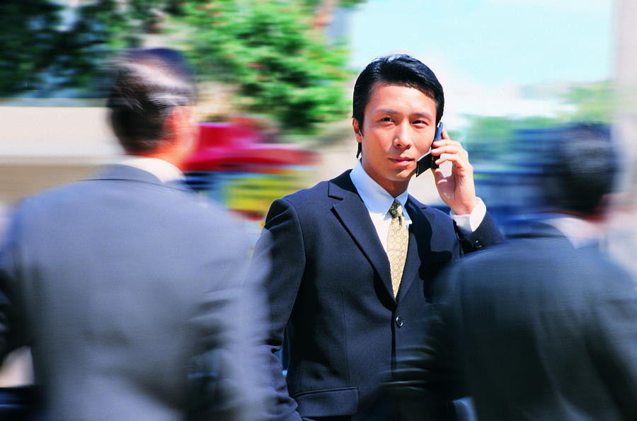 Businessman talking on phone, people rushing by Photograph by Photodisc