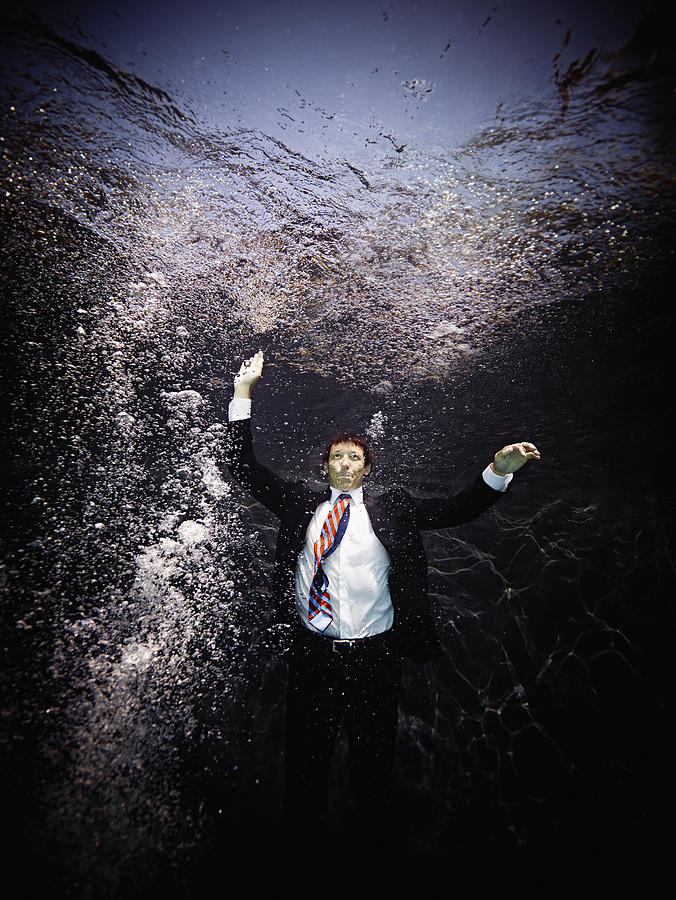 Businessman underwater in suit swimming to surface Photograph by Thomas Barwick