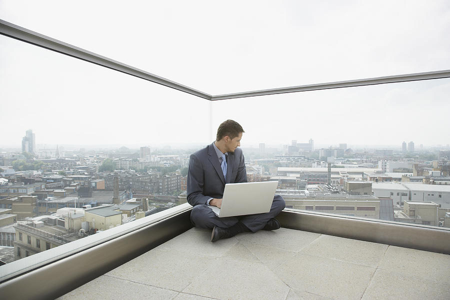 Businessman using laptop on rooftop Photograph by Justin Pumfrey