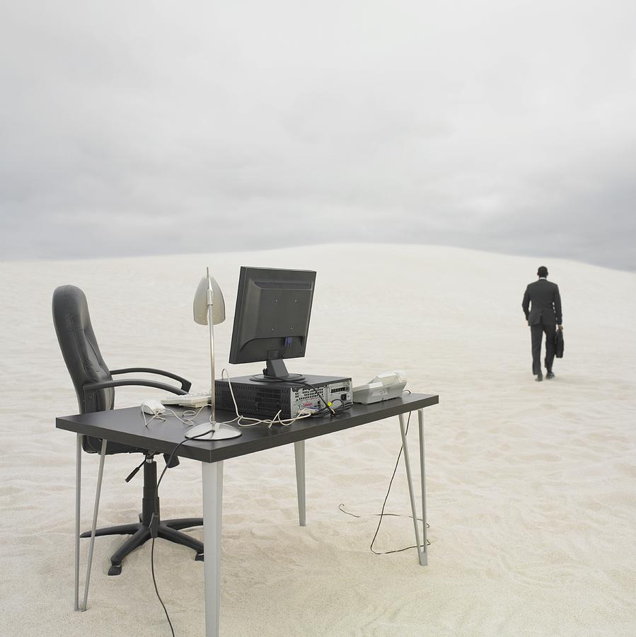 Businessman walking away from desk in the desert Photograph by Dave & Les Jacobs