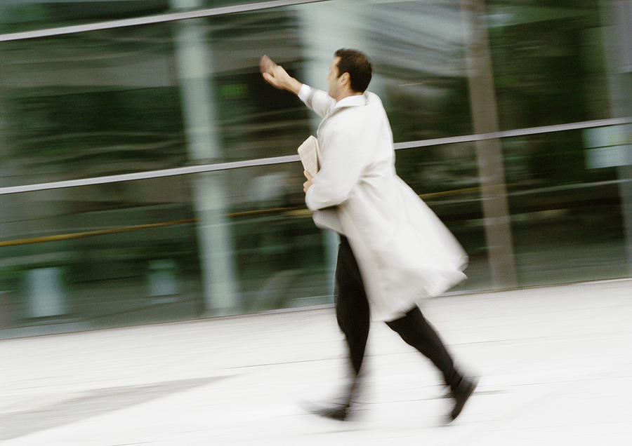 Businessman walking in street, hand raised, blurred Photograph by Eric Audras