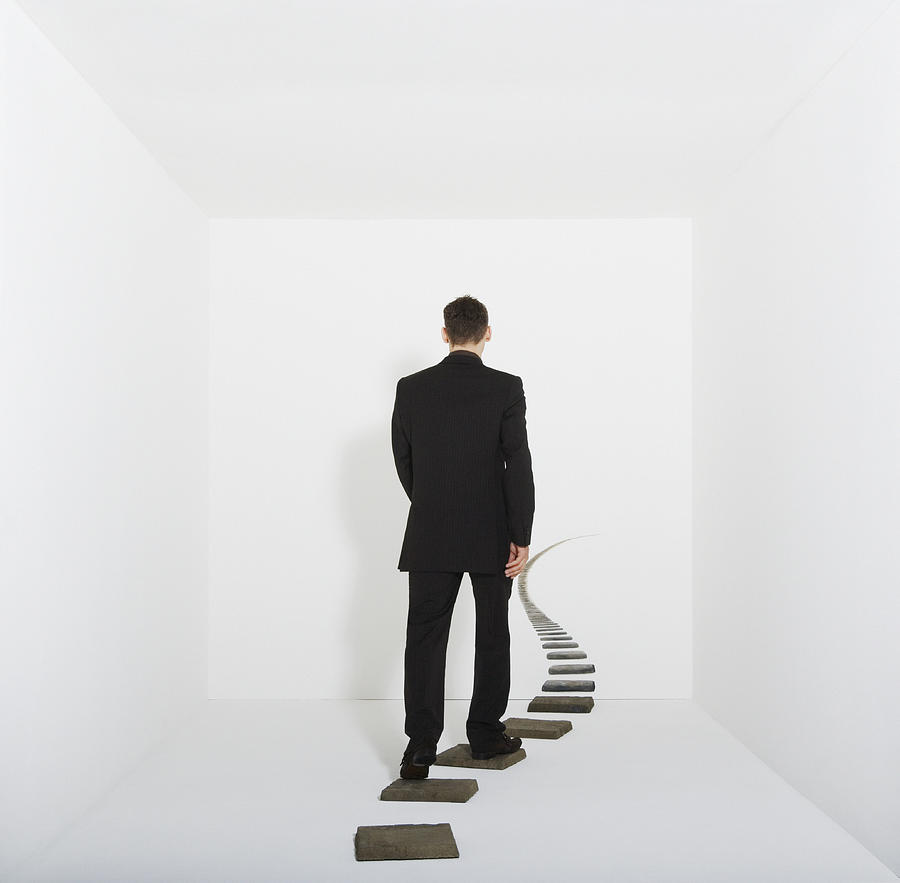 Businessman walking on stepping stones in white room, rear view Photograph by Anthony Harvie