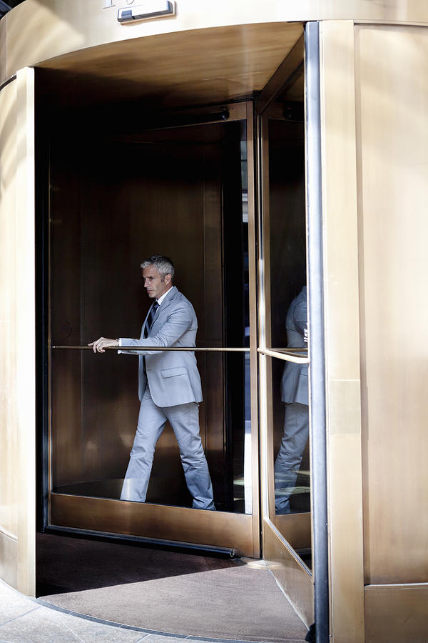 Businessman walking out of a revolving door. Photograph by Assembly