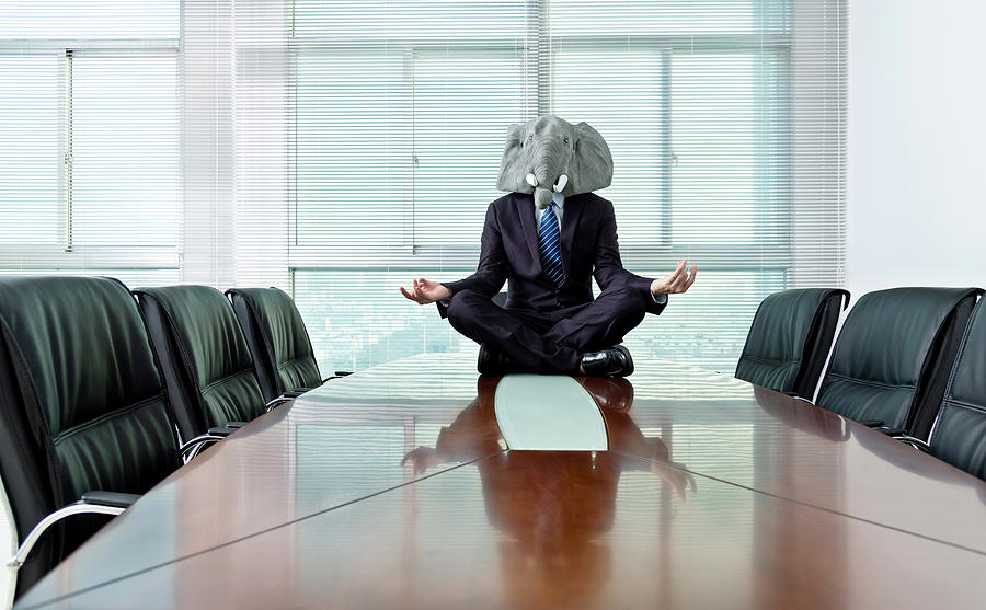 Businessman wearing a mask meditating on conference table Photograph by Baona