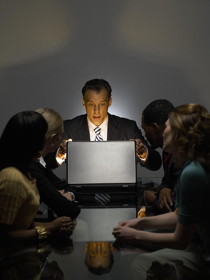 Businessman With Colleagues Sitting in a Dark Office Opening a Bright Briefcase Photograph by Digital Vision.