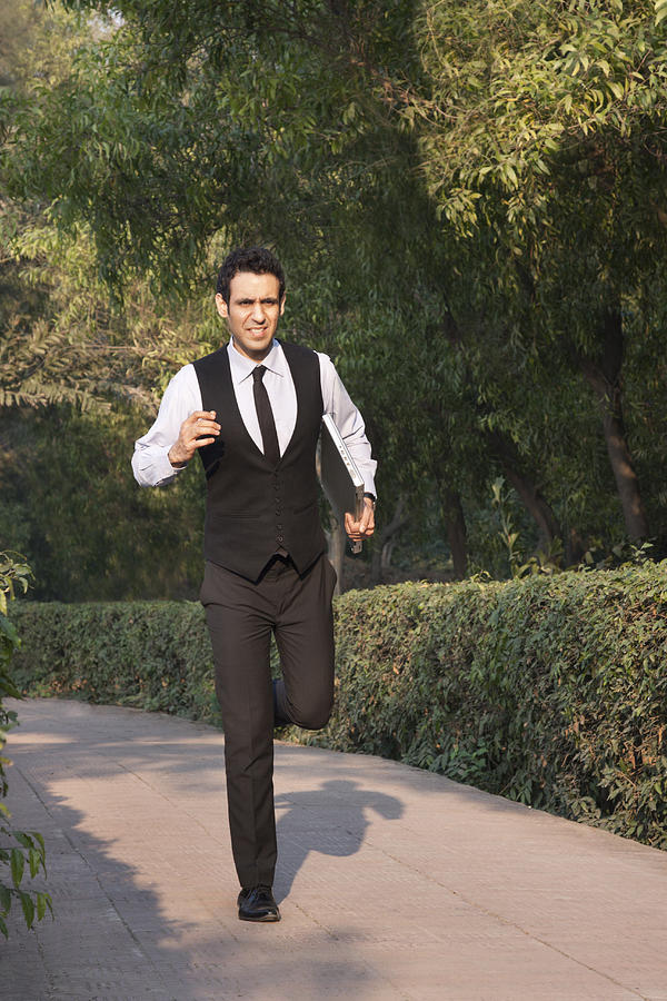 Businessman with laptop running in a park , INDIA , DELHI Photograph by IndiaPix/IndiaPicture
