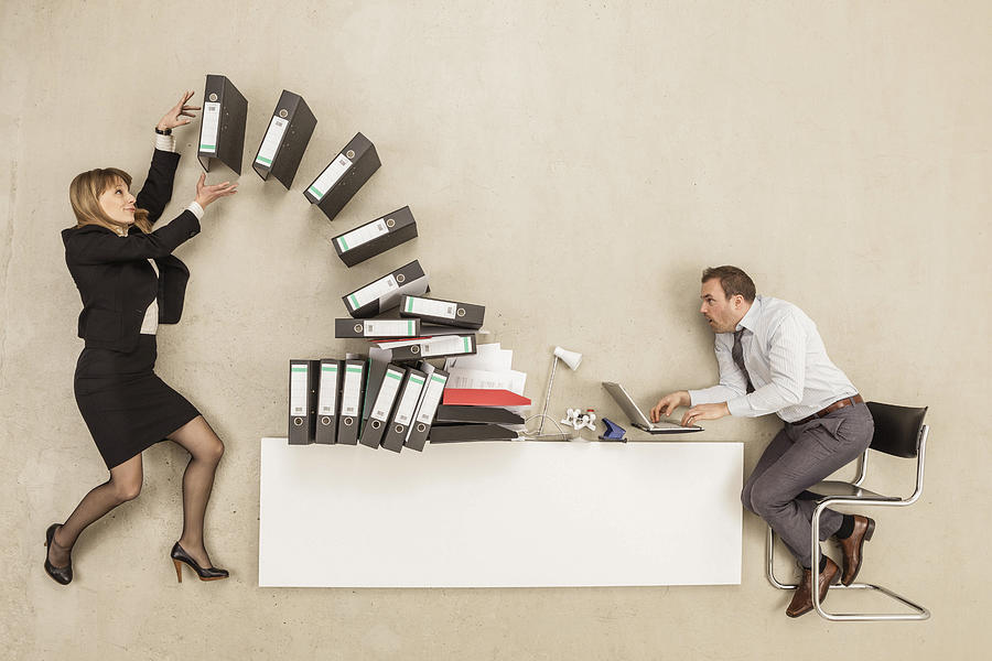 Businessman working on office desk while businesswoman providing stack of files Photograph by Westend61