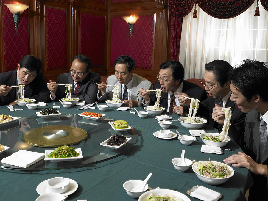 Businessmen at banquet table eating noodles Photograph by Hans Neleman
