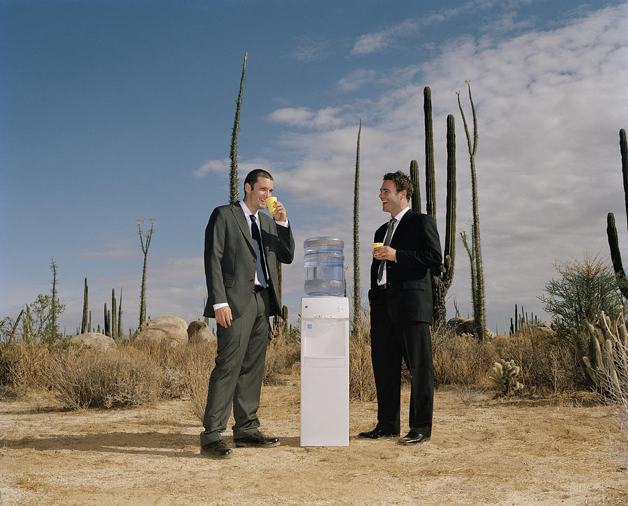 Businessmen chatting near water cooler in desert Photograph by Matthias Clamer