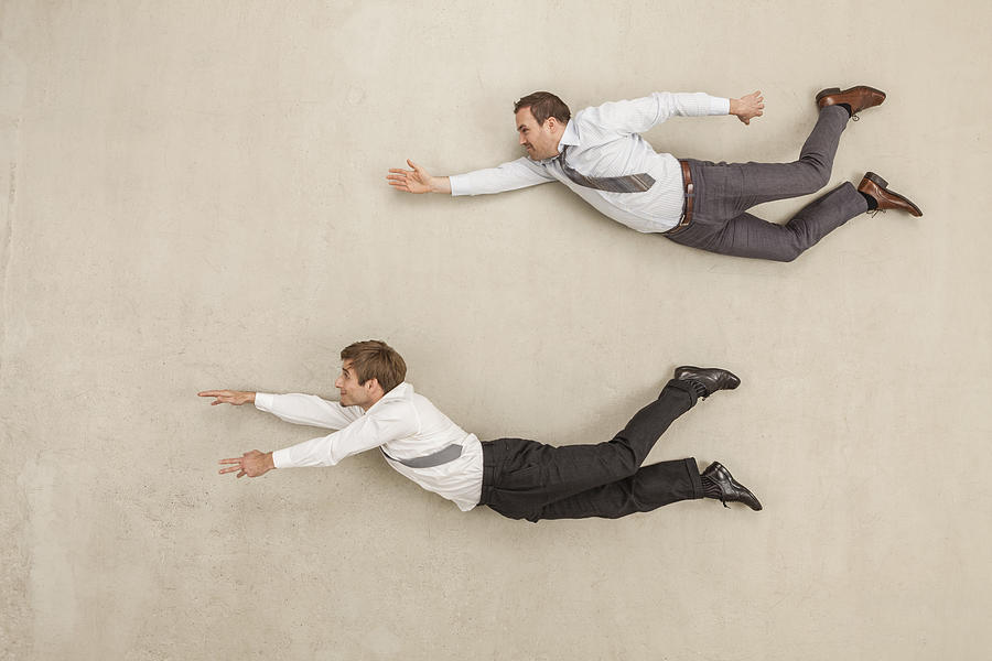 Businessmen flying against beige background Photograph by Westend61