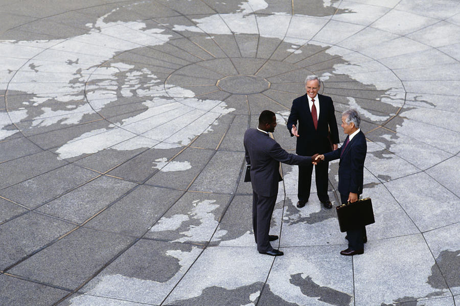 Businessmen shaking hands on map of globe Photograph by Jon Feingersh Photography Inc