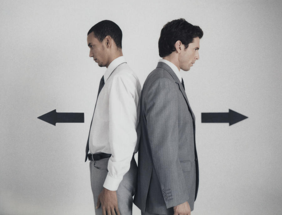 Businessmen standing back to back with arrow signs pointing in opposite directions Photograph by Matthieu Spohn