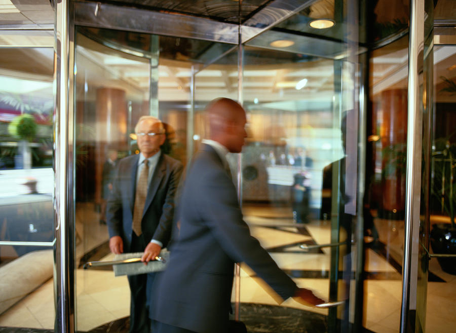 Businesspeople Walking Through a Revolving Door Photograph by Ryan McVay