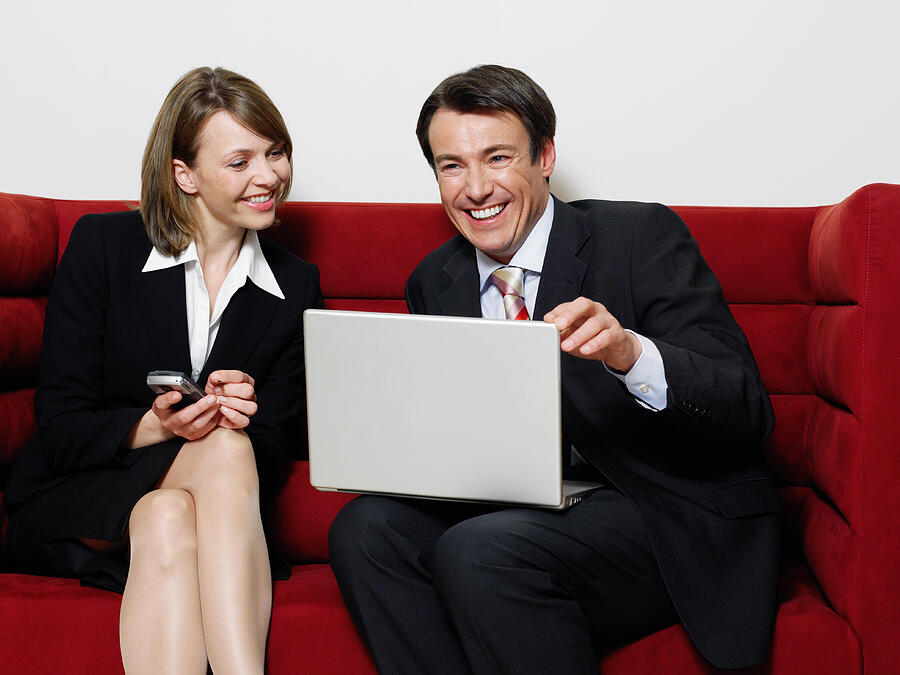 Businesswoman and Businessman Sitting on a Sofa With a Laptop Photograph by Digital Vision.