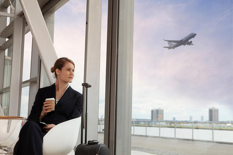 Businesswoman drinking coffee in airport Photograph by Image Source