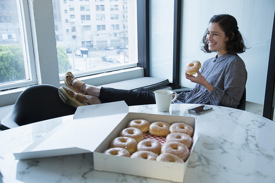 Businesswoman eating donut in conference room Photograph by Ronnie Kaufman