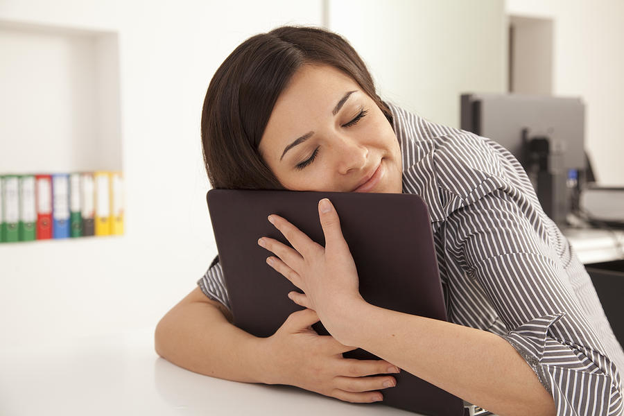 Businesswoman hugging computer in office Photograph by Robert Christopher