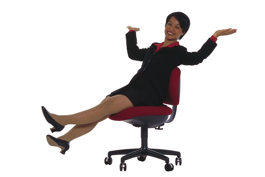 Businesswoman in office chair rolling across floor Photograph by Comstock