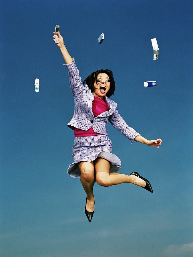 Businesswoman jumping with mobile phones in air, low angle Photograph by Mike Powell