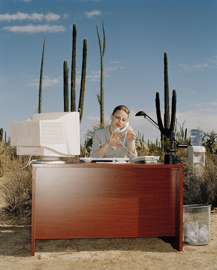 Businesswoman on telephone painting nails at desk in desert Photograph by Matthias Clamer
