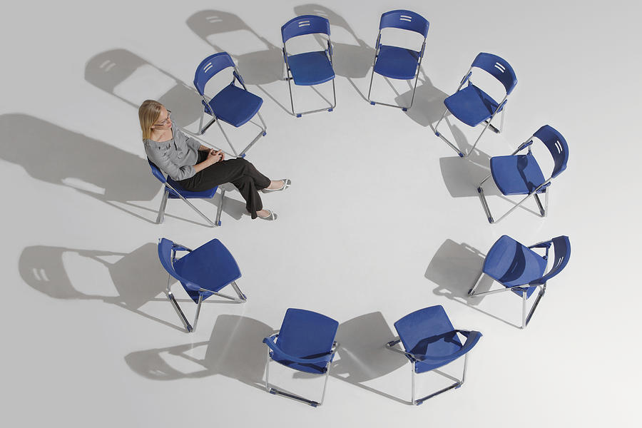 Businesswoman sitting alone in circle of chairs, elevated view Photograph by Symphonie