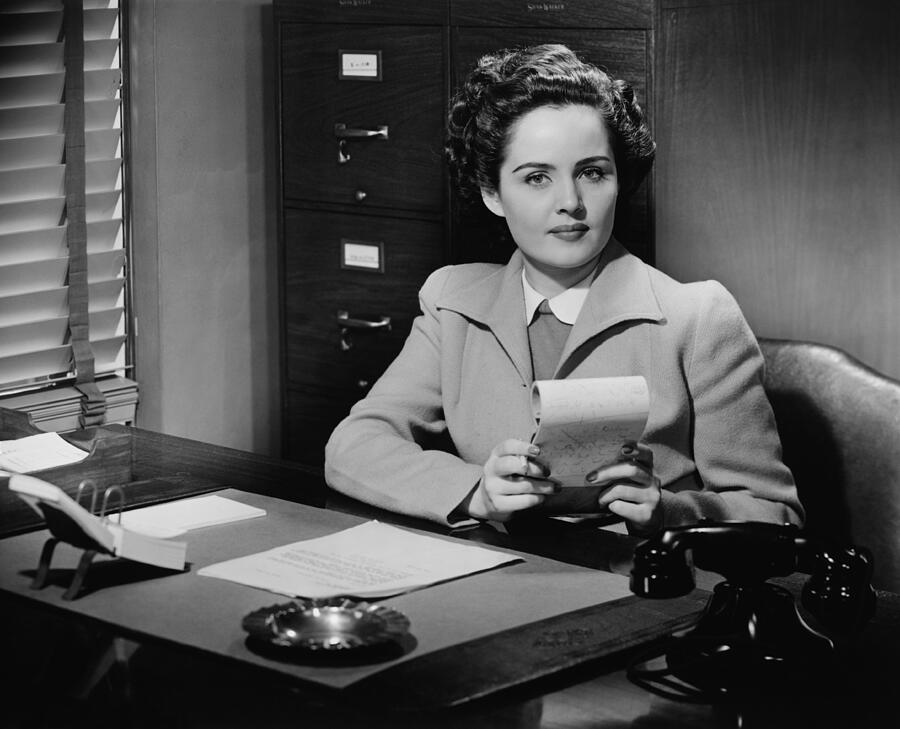 Businesswoman sitting at desk, holding notepad, (B&W), portrait Photograph by George Marks