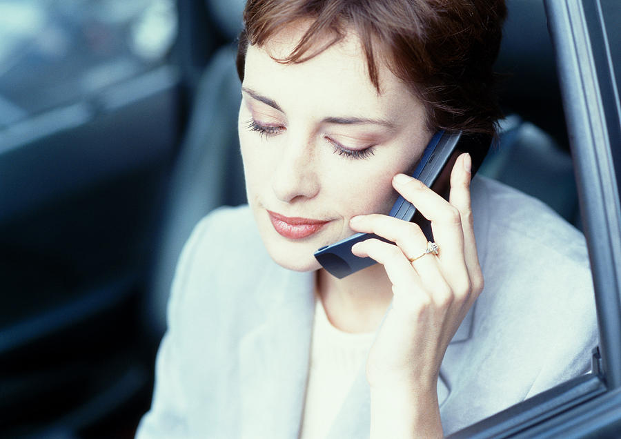 Businesswoman sitting in car, using cell phone Photograph by Eric Audras