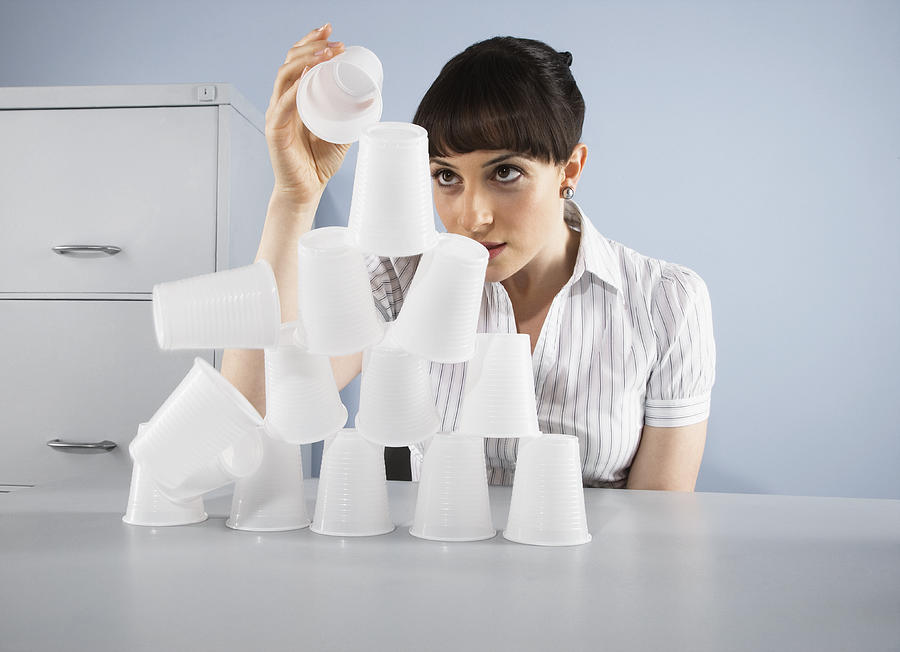 Businesswoman stacking plastic cups into pyramid Photograph by Anthony Lee