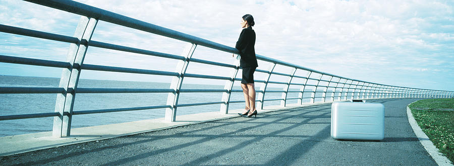Businesswoman standing next to railing, briefcase on ground, panoramic Photograph by Matthieu Spohn