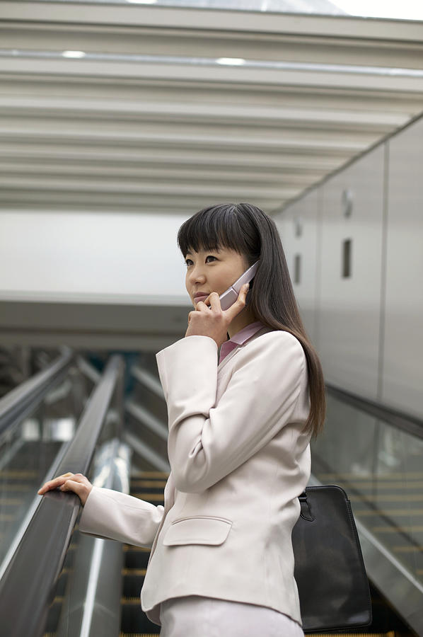 Businesswoman Standing on an Escalator Using a Mobile Phone Photograph by Digital Vision.