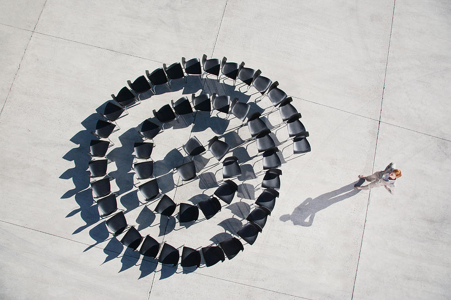 Businesswoman standing with spiral of office chairs Photograph by Martin Barraud