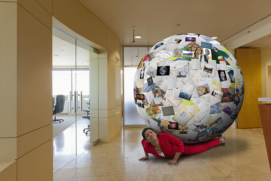 Businesswoman stuck underneath globe of images in office Photograph by John M Lund Photography Inc