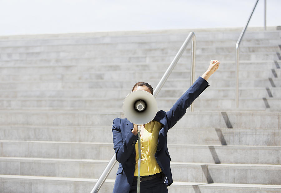 Businesswoman using megaphone on urban steps Photograph by Paul Bradbury