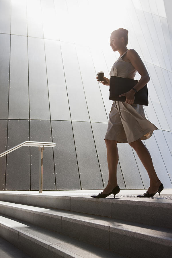 Businesswoman with coffee walking down steps outdoors Photograph by Tom Merton