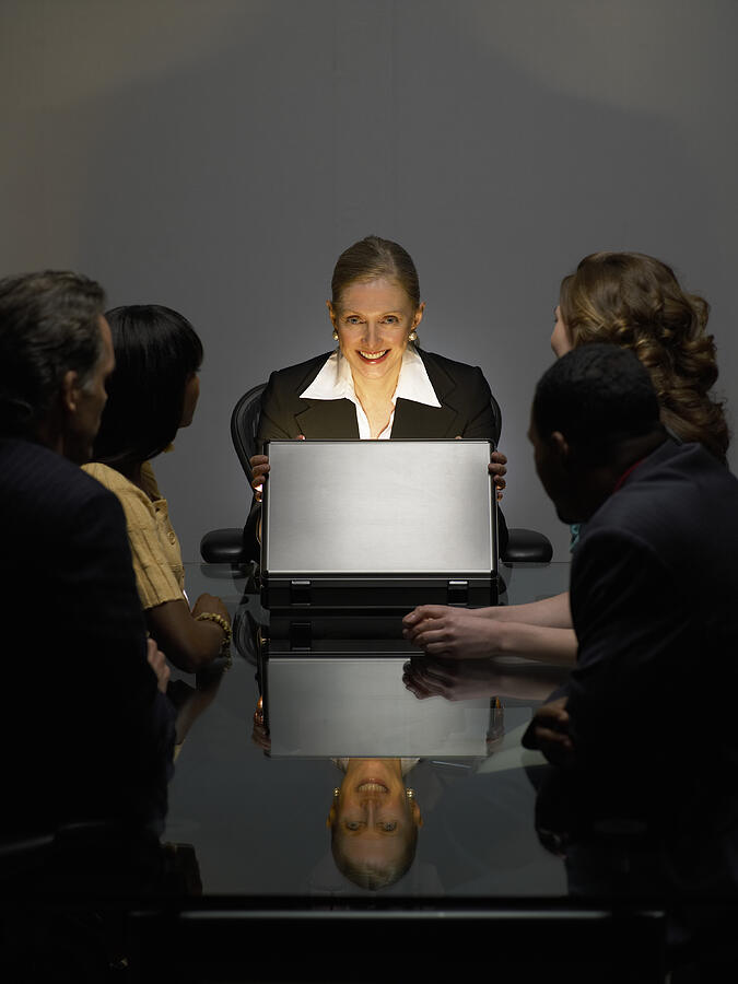 Businesswoman With Colleagues Sitting in a Dark Office Opening a Bright Briefcase Photograph by Digital Vision.
