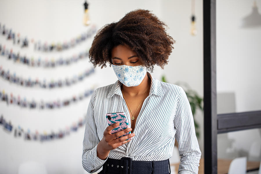 Businesswoman with face mask using mobile phone in office Photograph by Luis Alvarez