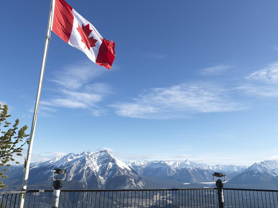 Canada, Alberta, Banff National Park, Canadian flag blowing above viewing deck, mountain range in background Photograph by Ascent/PKS Media Inc.