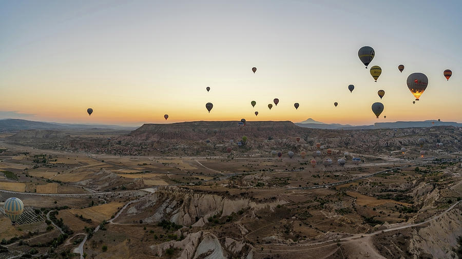Cappadocia, Turkey - Wide angle Panorama aerial shot of colorful hot air balloons together floating in the sky at early morning in Goreme against volcanic hills Photograph by Arpan Bhatia