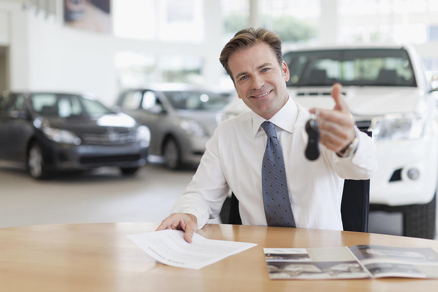 Car salesman handing keys over desk Photograph by Photo_Concepts