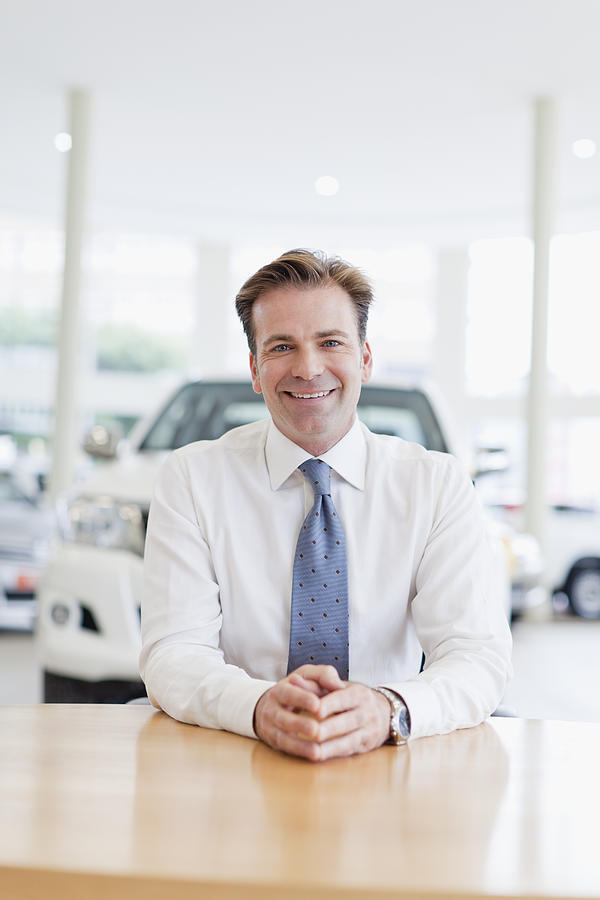 Car salesman smiling at desk Photograph by Photo_Concepts