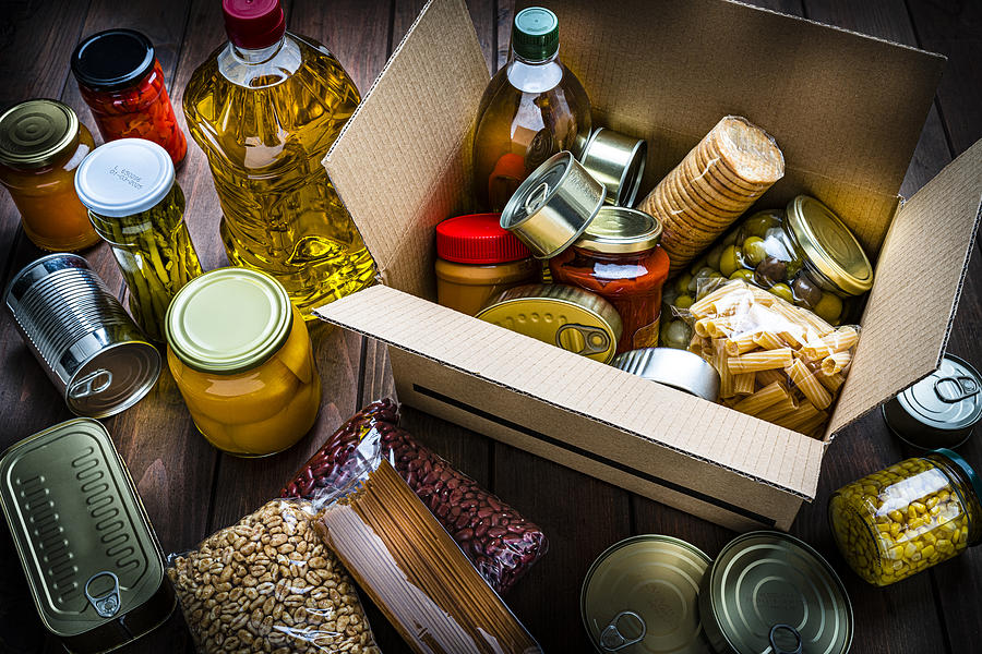Cardboard box filled with non-perishable foods on wooden table. High angle view. Photograph by Fcafotodigital