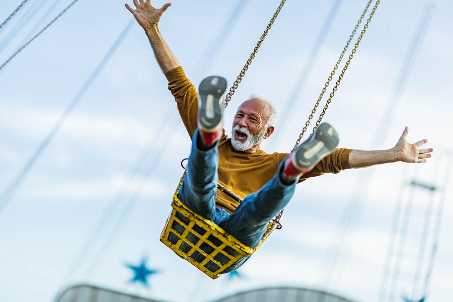 Carefree mature man having fun on chain swing ride in amusement park. Photograph by Skynesher